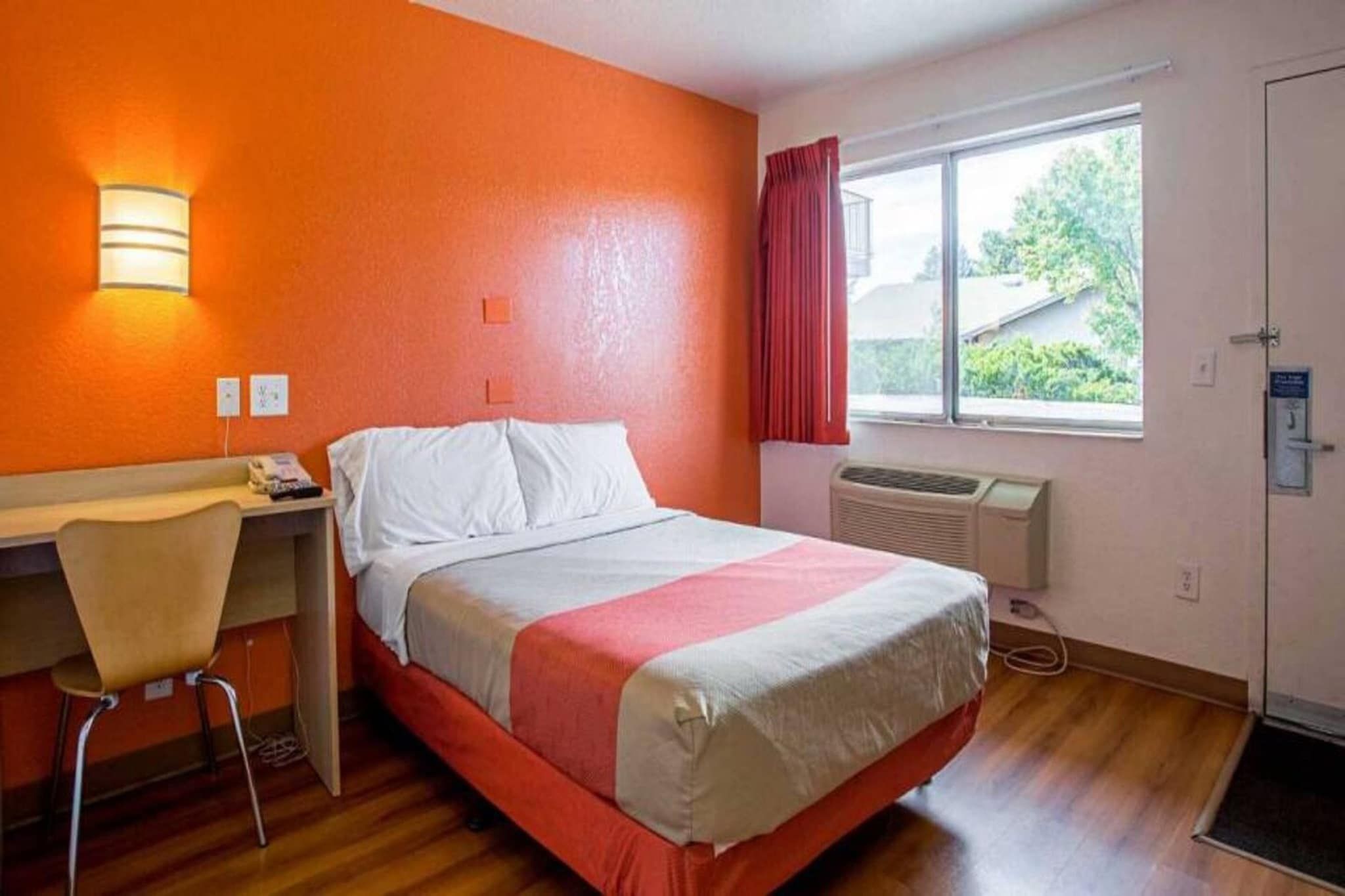 Ein Hotelzimmer mit Bett, Schreibtisch, Stuhl, einem Fenster mit Vorhängen und einem Heizkörper.