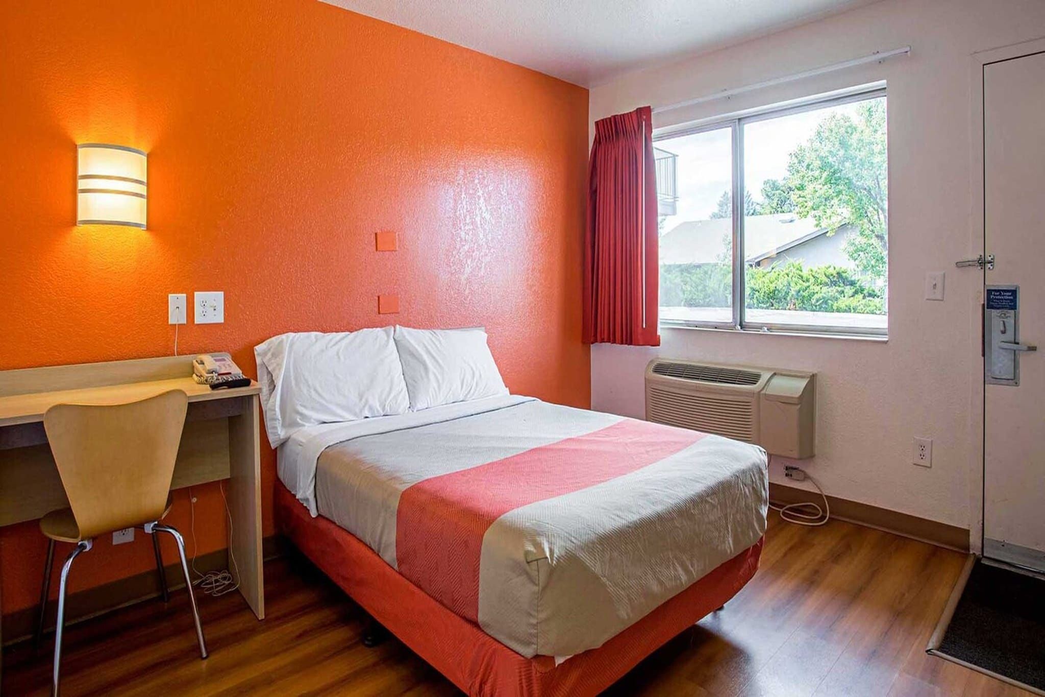A hotel room with a bed, a desk, a chair, a window with a view, and a door.