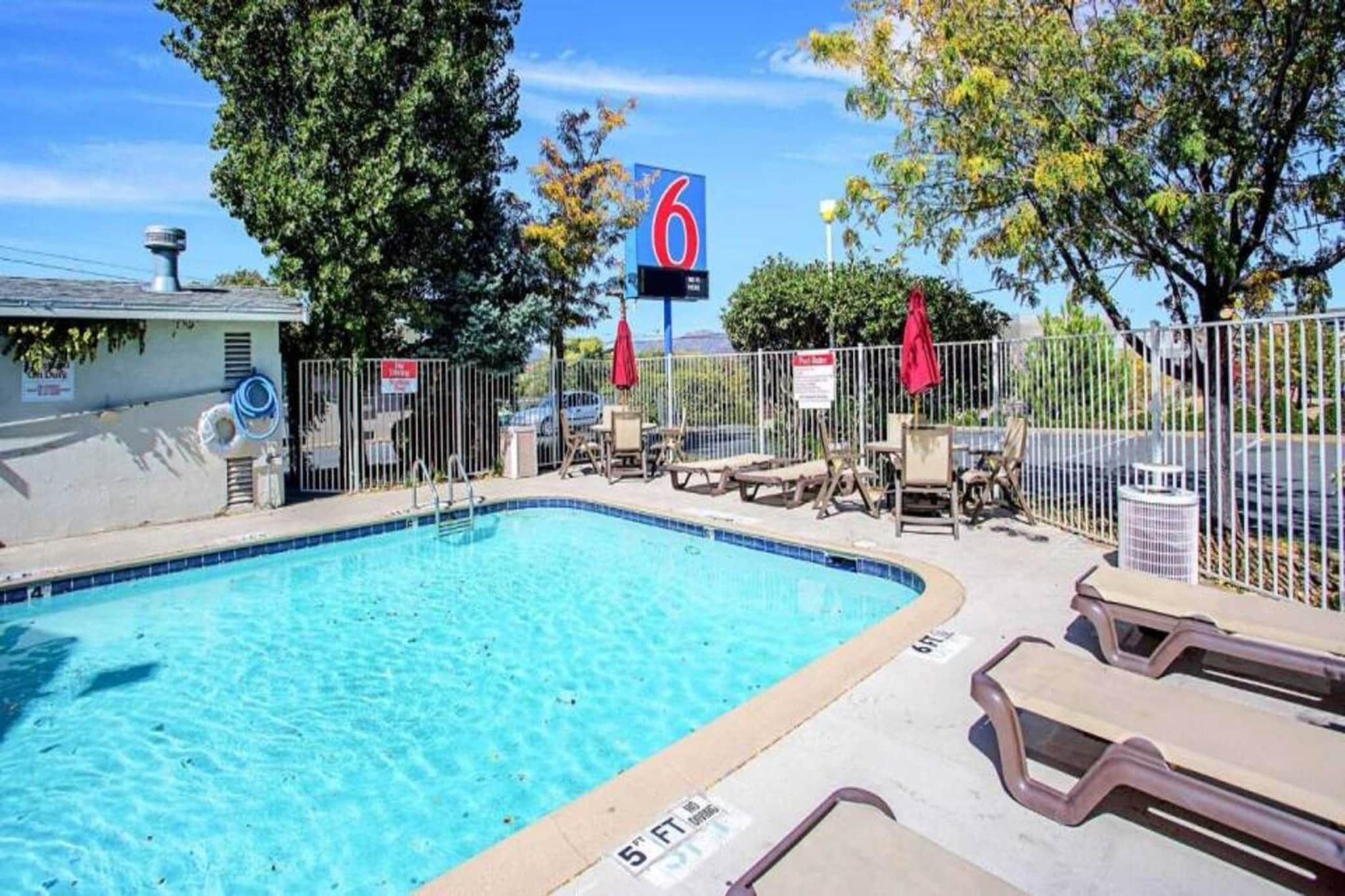 Une piscine avec des chaises longues et un espace délimité par une clôture, un panneau indiquant le numéro 6, et un ciel dégagé.