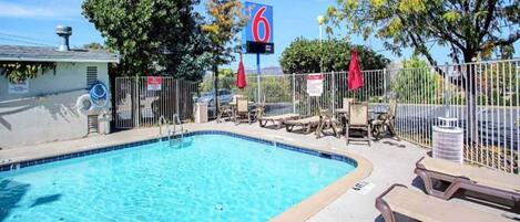 A swimming pool with lounge chairs and a fenced area, a sign with the number 6, and a clear sky.