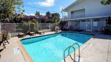 Une piscine rectangulaire avec un escalier en métal au premier plan, entourée d’une clôture blanche.