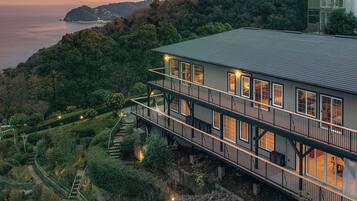 A multi-story building with a balcony, surrounded by lush greenery and overlooking a body of water.