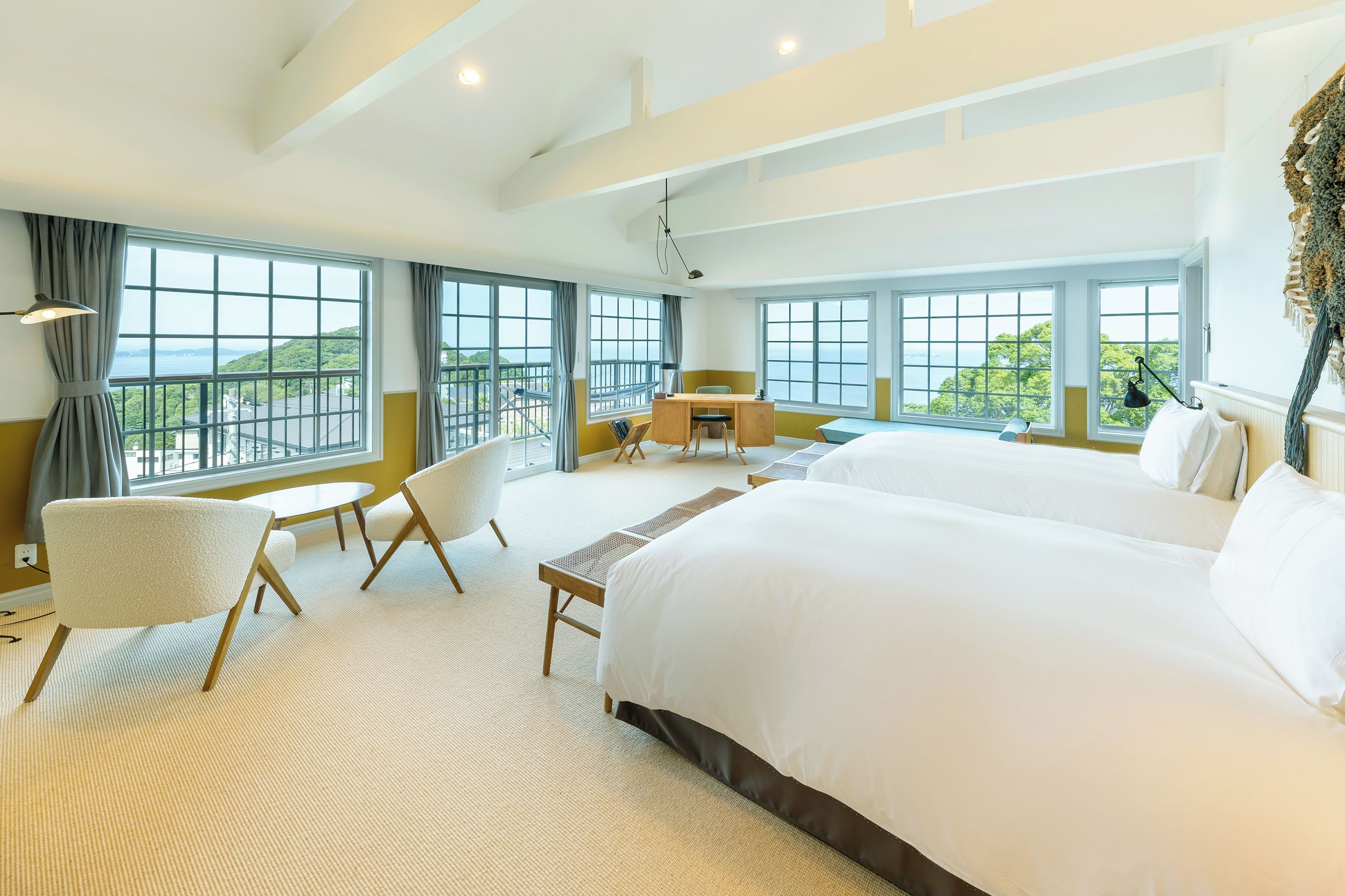 A hotel room with two large beds, a desk, a chair, and a view of the sea.
