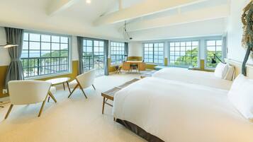 A hotel room with two large beds, a desk, a chair, and a view of the sea.