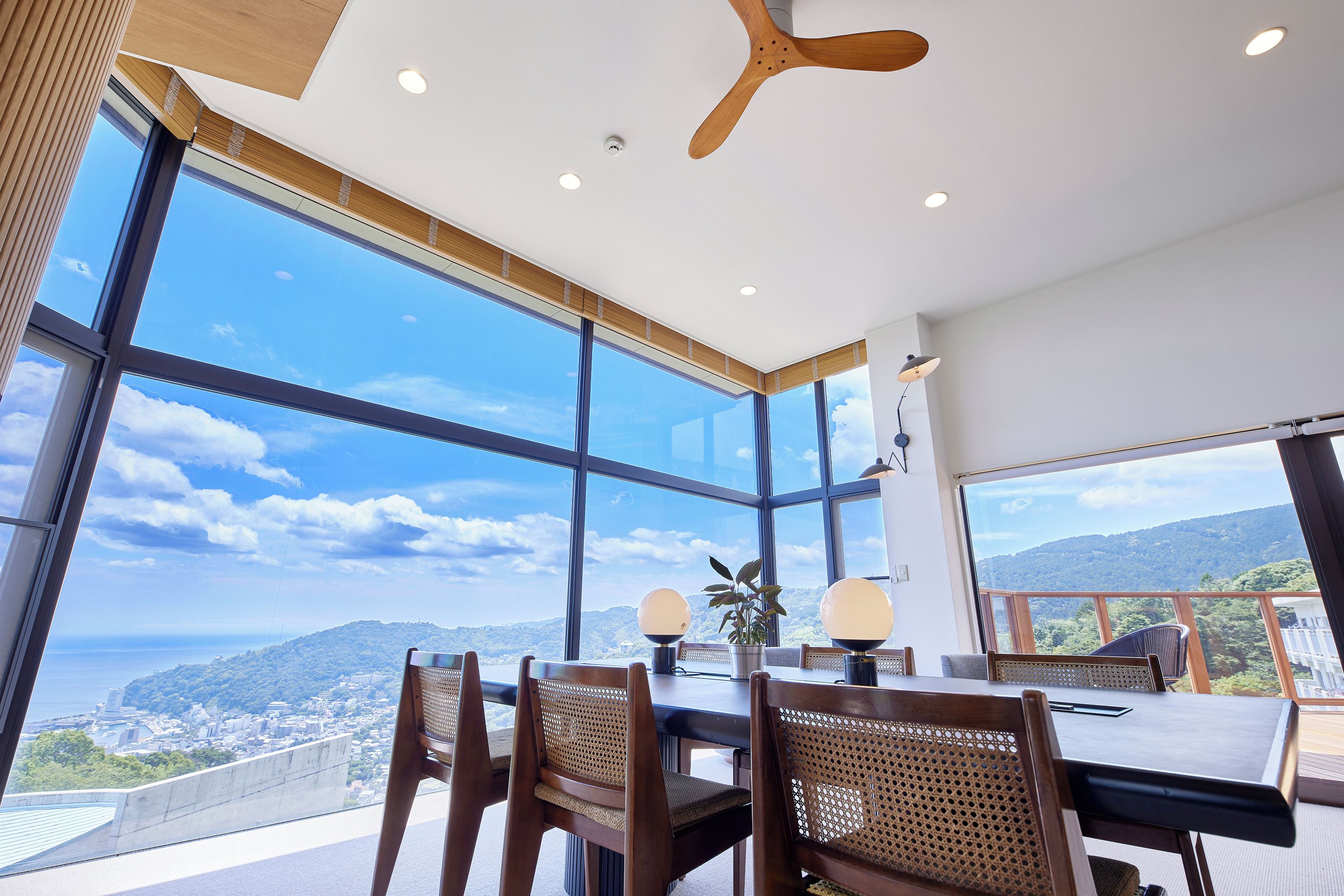 A modern interior with large windows offering a city view, a dining table with chairs, and a ceiling fan.
