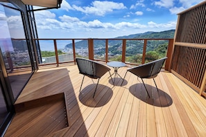 A wooden deck with two chairs and a table, overlooking a coastal cityscape. - GLAMDAY ATAMI (Atami)
