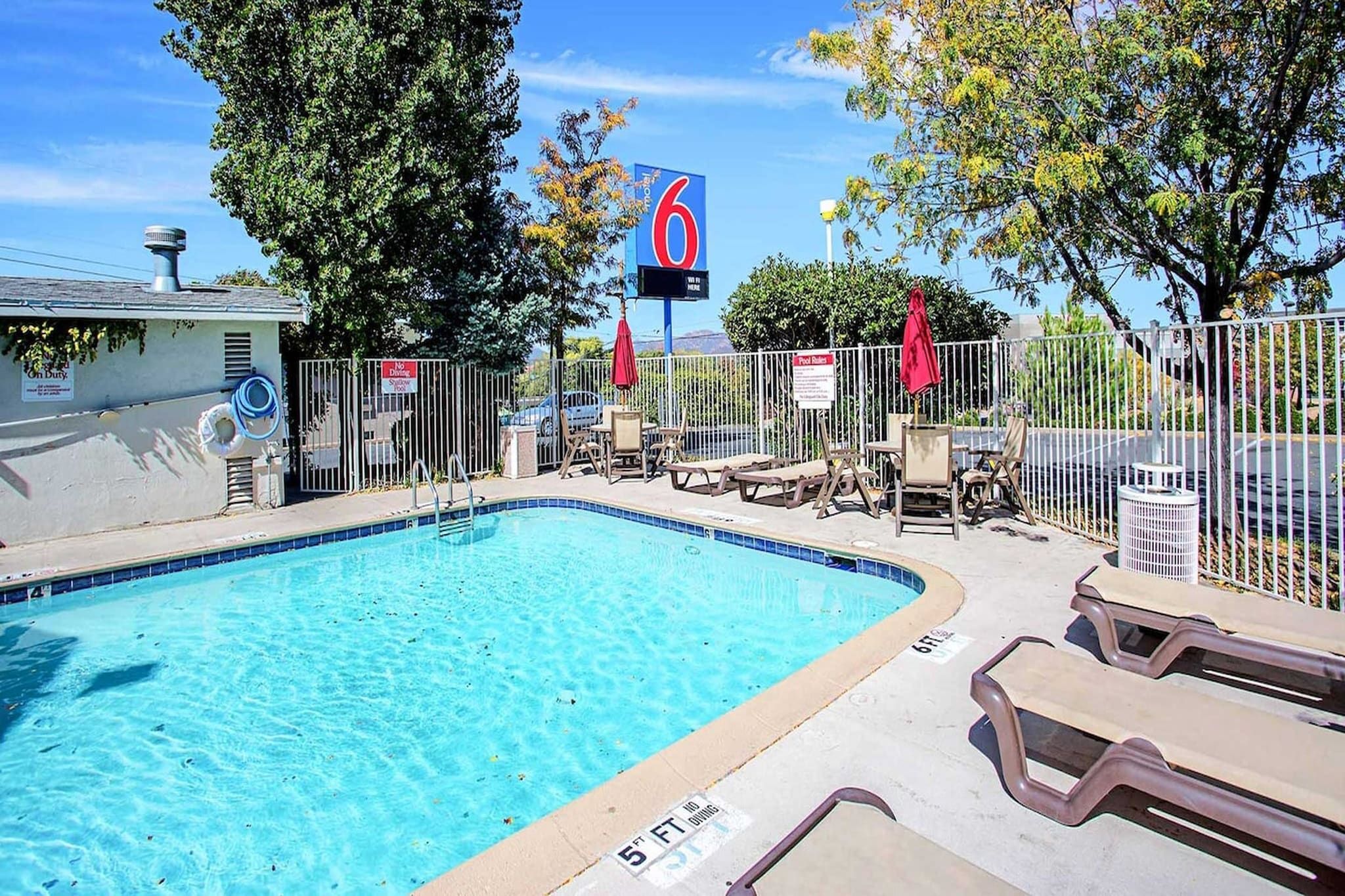 A swimming pool with lounge chairs and umbrellas, surrounded by a fence and trees.