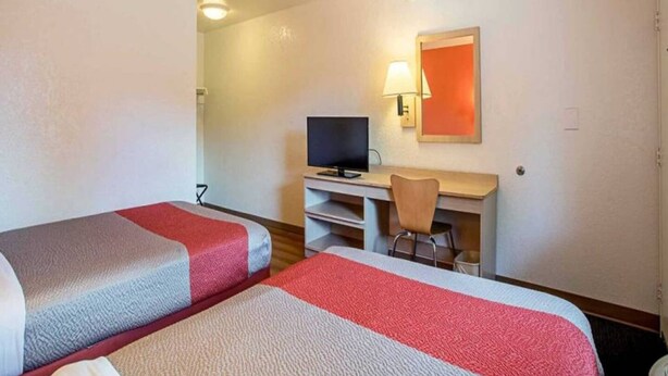 Ein Hotelzimmer mit zwei Betten, einem Schreibtisch mit Computer, einem Stuhl und einem Fernseher.
