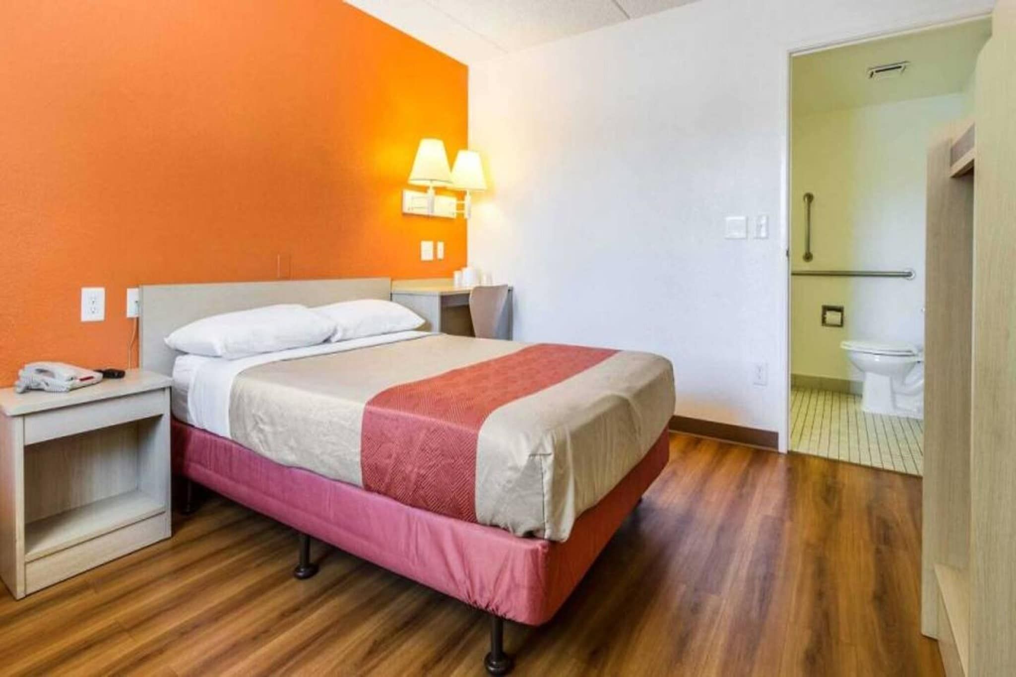 A hotel room with a bed, bedside table, lamp, and a view of the bathroom.
