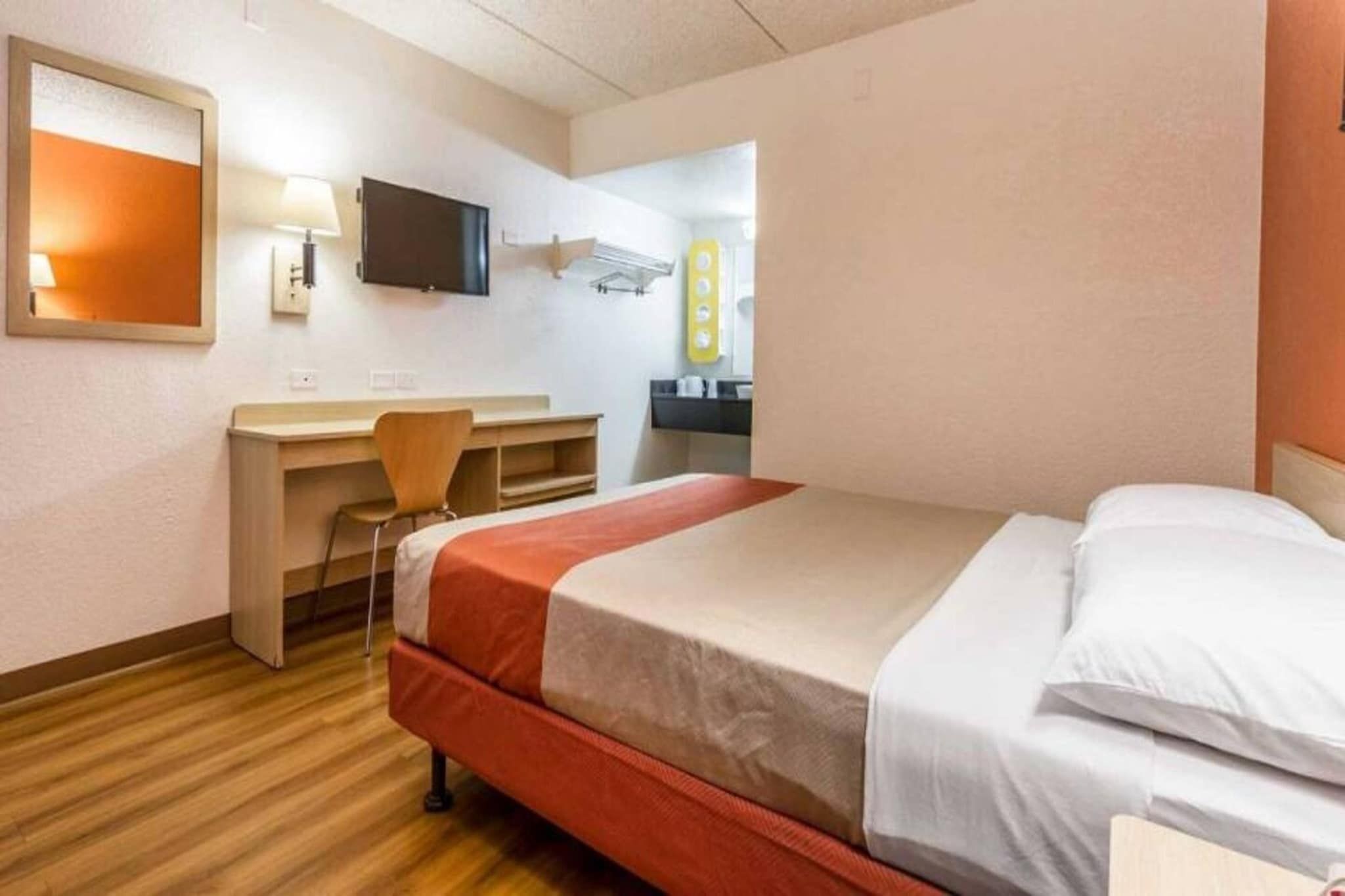 Ein Hotelzimmer mit Bett, Schreibtisch, Stuhl, Fernseher und Spiegel.