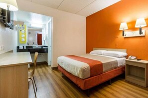 Una habitación de hotel con una cama, mesita de noche y escritorio con silla.