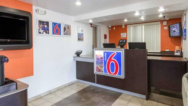 Ein Hotel-Empfangsbereich mit einem großen Schild mit der Zahl 6, einem an der Wand montierten Fernseher und einer Rezeption mit digitaler Anzeige.