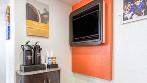 Ein Zimmer mit einer Kaffeemaschine, einem an einer orangefarbenen Wand montierten Fernseher und einem gerahmten Bild.