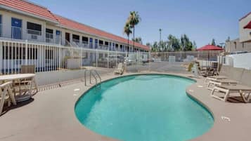 A swimming pool with a fenced area, lounge chairs, and a building with a red roof in the background.
