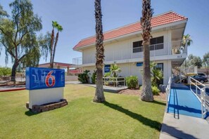 Un edificio de dos pisos con techo de tejas rojas, un letrero que indica la habitación número 6 y un área de piscina.
