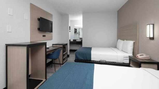 Ein Hotelzimmer mit Schreibtisch, zwei Betten, Fernseher und einem im Hintergrund sichtbaren Badezimmer.