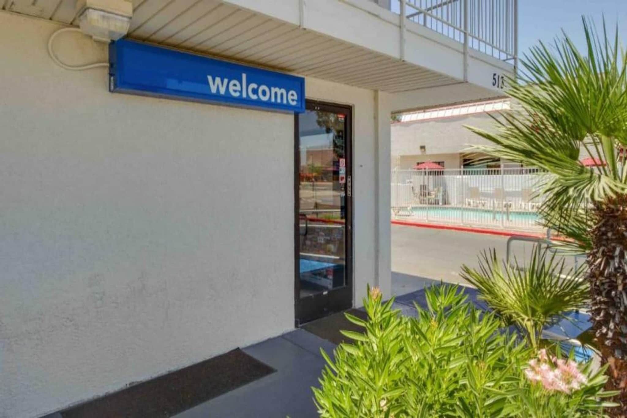 Ein Gebäudeeingang mit einem 'welcome'-Schild, einer Glastür und einem Poolbereich, der durch das Glas sichtbar ist.