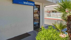 Ein Gebäudeeingang mit einem 'welcome'-Schild, einer Glastür und einem Poolbereich, der durch das Glas sichtbar ist.