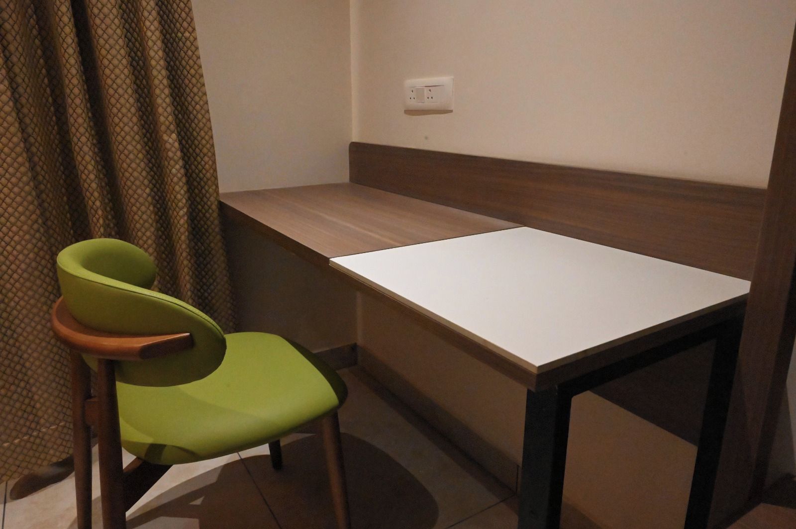 Una habitación pequeña con una sola silla verde, una mesa blanca y una pared marrón.