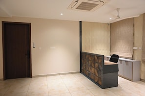 A hotel room with a wooden door, a reception desk, a ceiling fan, and a window with a blind. - LE PRESTIGE RESIDENCY Tindivanam (Tindivanam)