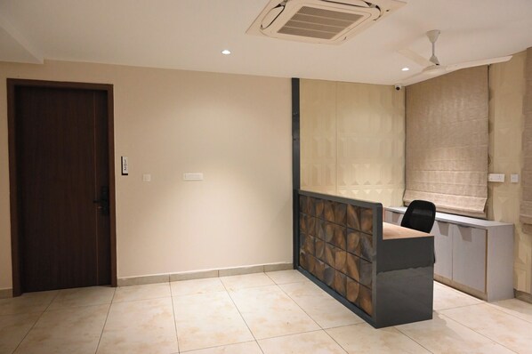 Habitación de hotel con puerta de madera, mostrador de recepción, ventilador de techo y ventana con persiana.