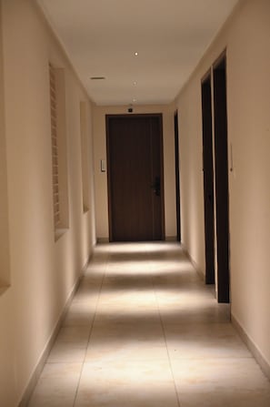 Un pasillo con una puerta al final, una lámpara en el techo y suelo de baldosas.