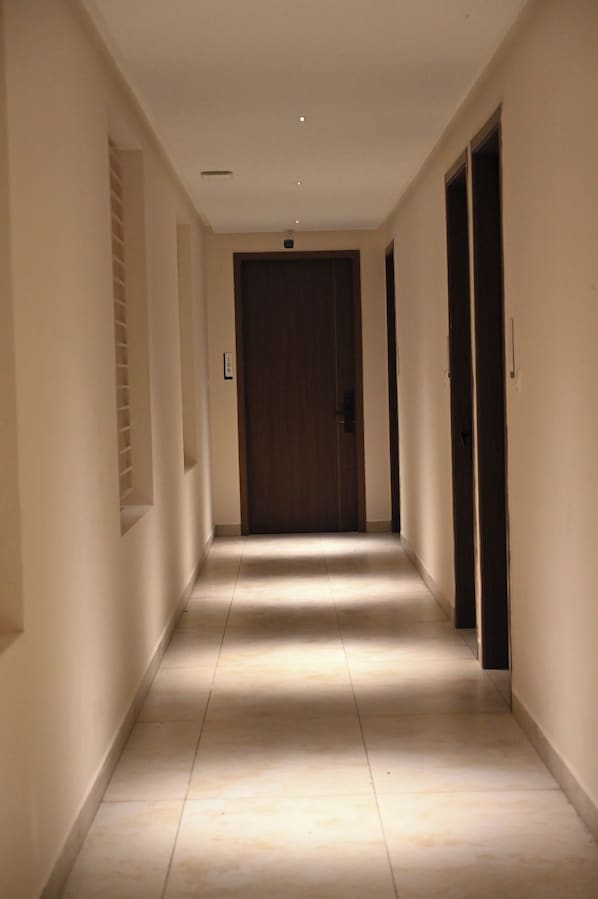 A corridor with a door at the end, a light fixture on the ceiling, and a tiled floor. - LE PRESTIGE RESIDENCY Tindivanam (Tindivanam)