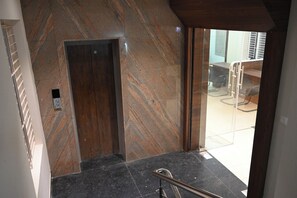 Un ascensor moderno con pared de mármol y puerta de vidrio que da acceso a una sala de estar.
