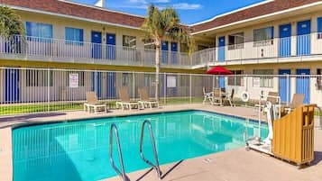 A hotel with a swimming pool, outdoor seating, and a fenced balcony area.
