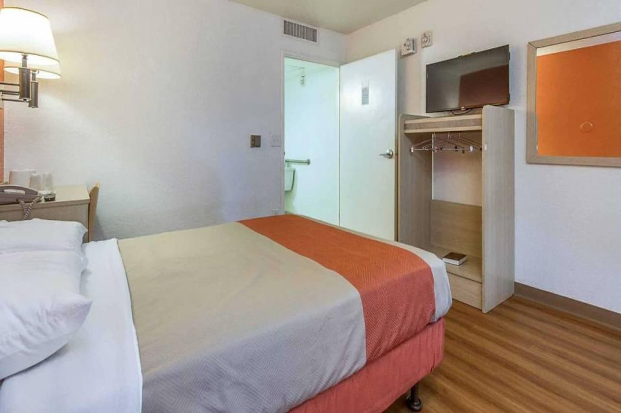 Ein Hotelzimmer mit einem Bett, einem Schreibtisch mit Telefon, einem Kleiderschrank und einem Fernseher.