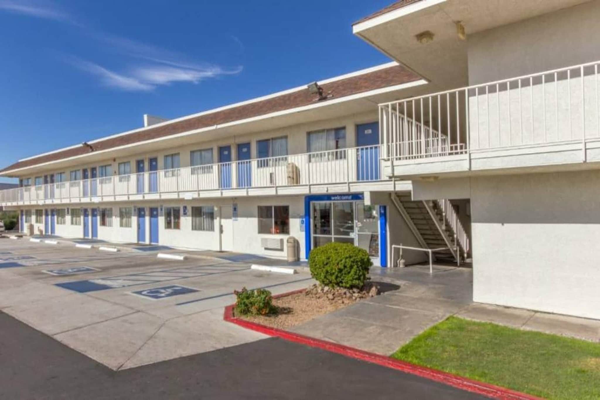 A motel with a parking lot, a small landscaped area, and a staircase leading to a balcony.