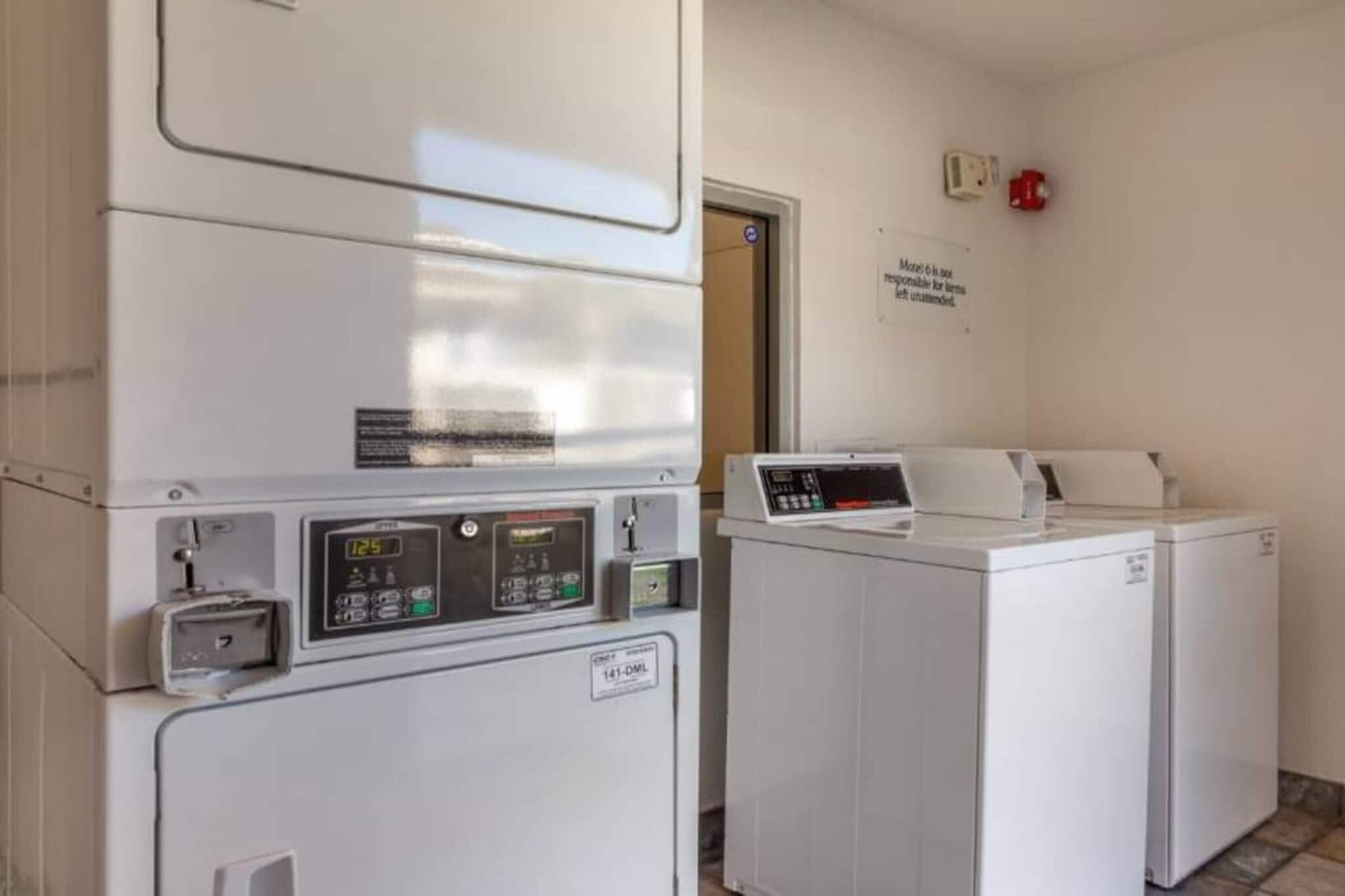 A laundry facility with a washing machine and dryer, a control panel, and a sign on the wall.