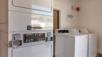A laundry facility with a washing machine and dryer, a control panel, and a sign on the wall.
