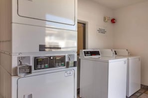 Een wasserette met een wasmachine en droger, een bedieningspaneel en een bord aan de muur.