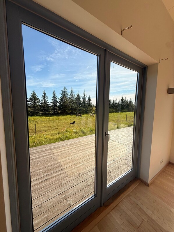 A room with a large sliding glass door leading to an outdoor deck with a wooden floor and a view of a grassy field and trees.