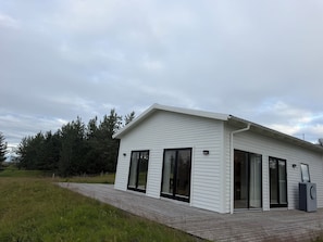 A modern house with a sloped roof, large sliding glass doors, and a covered porch. - Marvelous 3-bedroom farmhouse in charming Rangárþing ytra south Iceland (Rangárþing ytra)