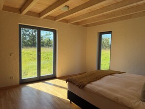 A bedroom with a bed, large windows, and a view of greenery.