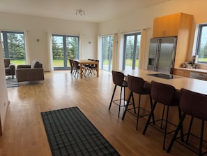 A modern kitchen with a large island, bar stools, and a dining area with a table and chairs. - Marvelous 3-bedroom farmhouse in charming Rangárþing ytra south Iceland (Rangárþing ytra)