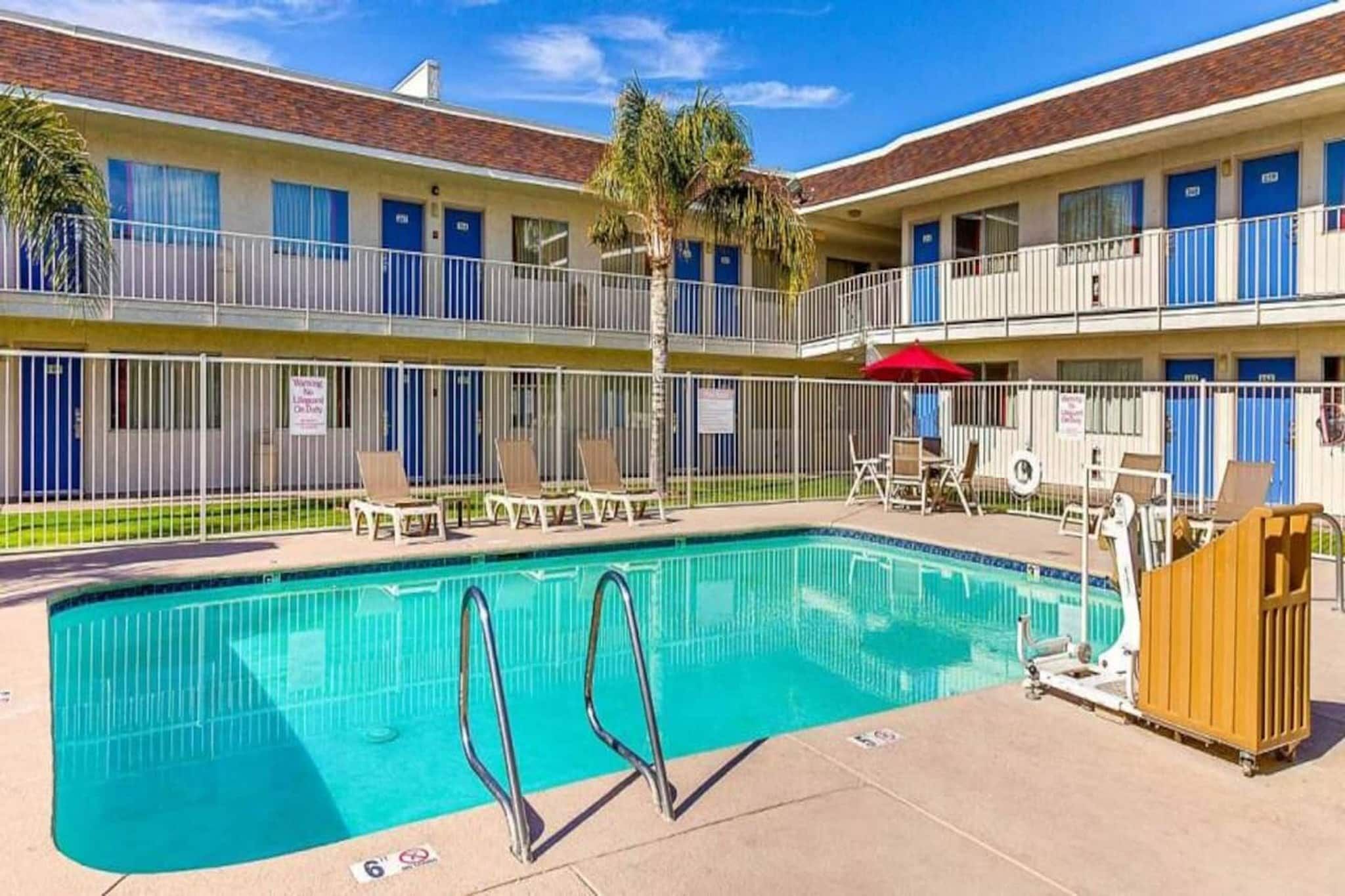 A hotel with a swimming pool, outdoor seating, and a fenced balcony area.