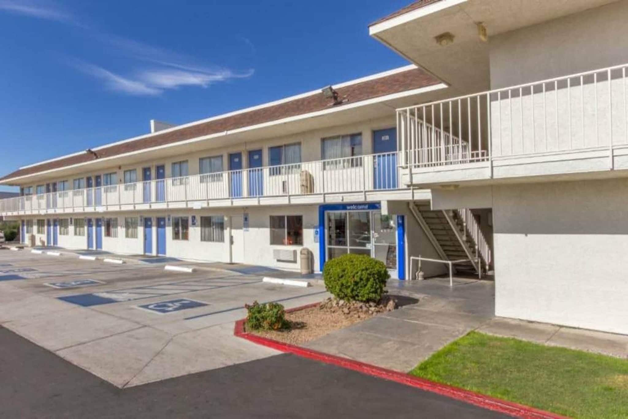 A motel with a parking lot, a small landscaped area, and a staircase leading to a balcony.