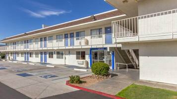 A motel with a parking lot, a small landscaped area, and a staircase leading to a balcony.
