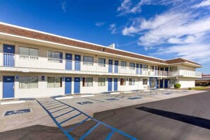 Un motel con estacionamiento, plazas de aparcamiento reservadas para personas con discapacidad y un edificio con varias puertas y ventanas.