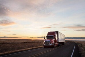 A red semi-truck driving on a road with a sunset in the background. - 2 Full Beds | Mini Fridge (Tempe)