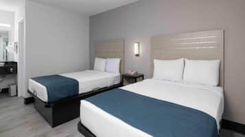A hotel room with two beds, a small table, a nightstand, and a mirror.