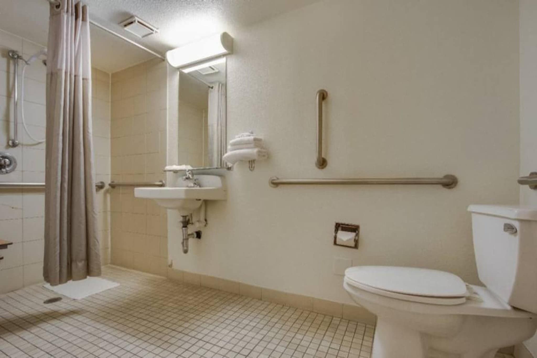 A standard bathroom with a shower, sink, toilet, and grab bars.