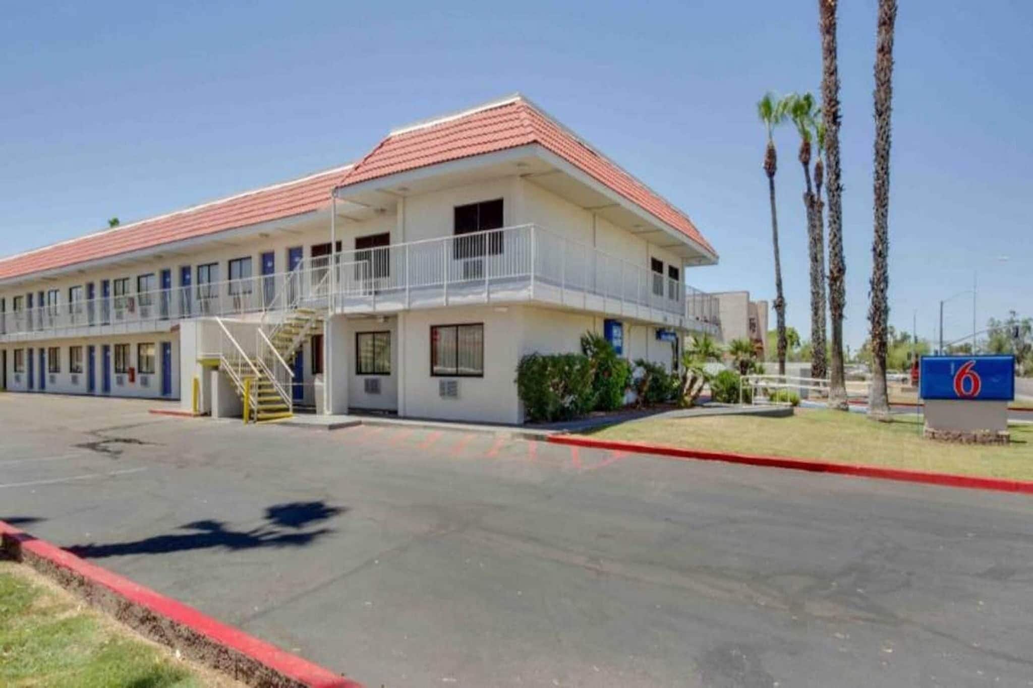 A two-story motel with a red roof, a covered parking area, and a sign indicating the number 6.