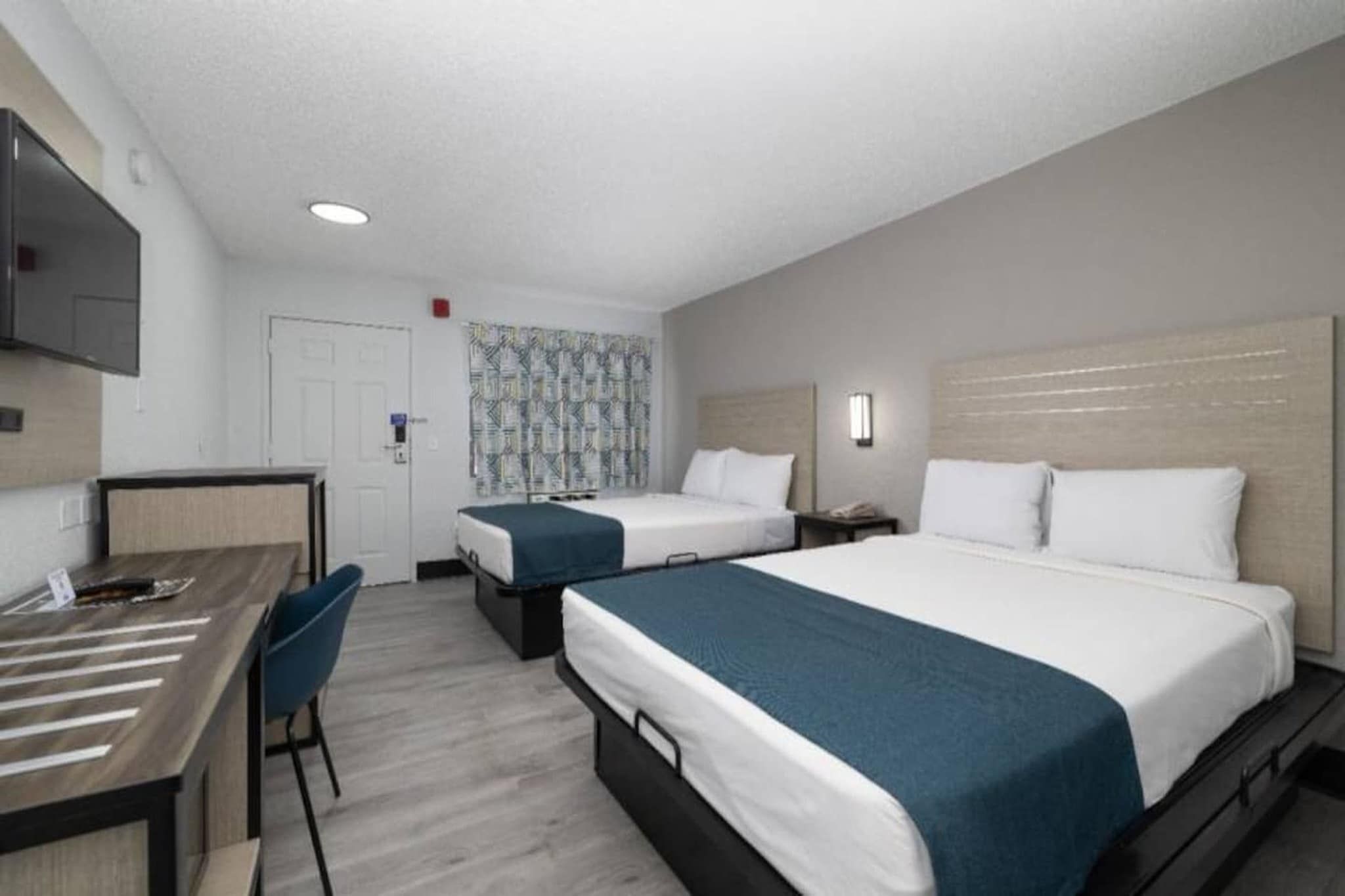 A hotel room with two beds, a desk, and a chair.