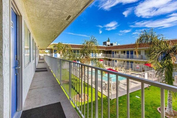 A hotel corridor with a pool area, outdoor seating, and a clear sky.