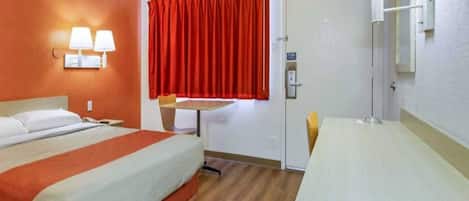 Een hotelkamer met een bed, een bureau, een stoel, een raam met rode gordijnen en een wandlamp.