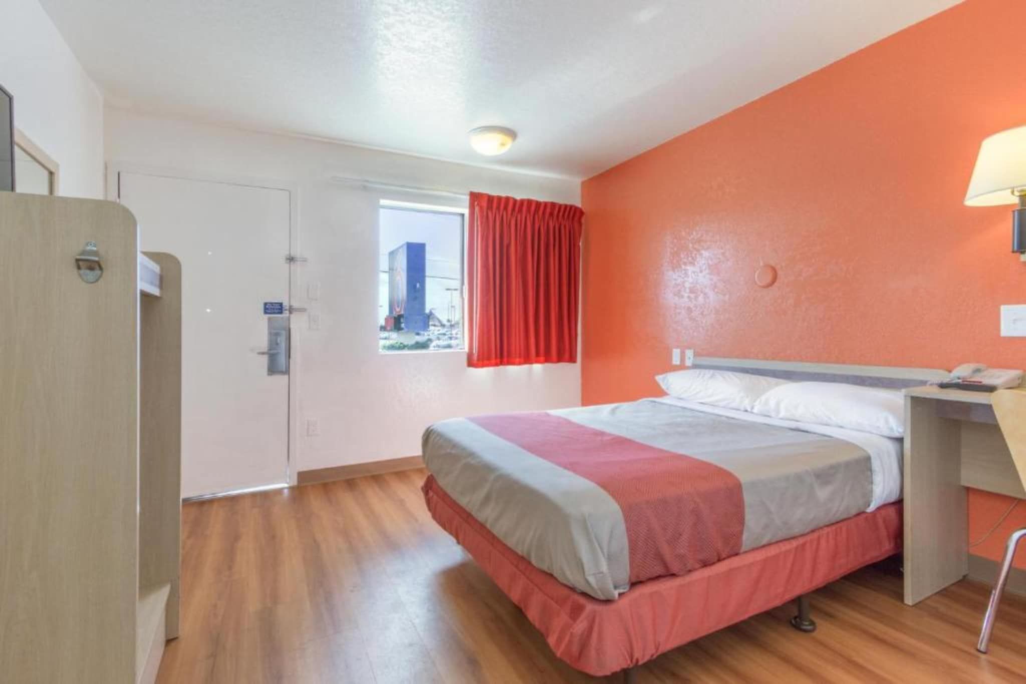 Ein Hotelzimmer mit Bett, Schreibtisch, einem Fenster mit Vorhängen und einer Tür.